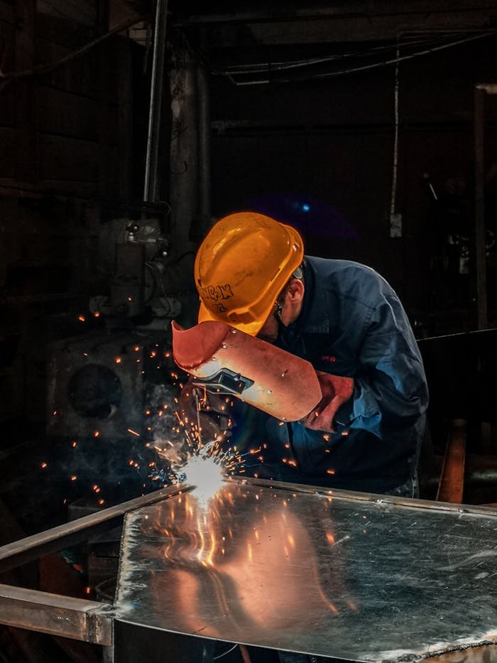 Servicios soldadura en Creixell. A welder wearing protective gear works on metal in an industrial workshop, surrounded by sparks.