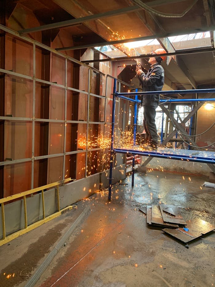 Servicios soldadura en Creixell. A construction worker welds metal indoors, creating flying sparks in a factory setting.